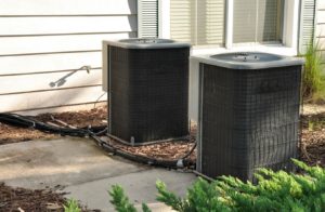 Two air conditioning units outside of a white paneled house